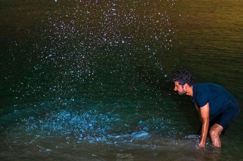 A person in a blue shirt crouching near a body of water with light reflections. 2