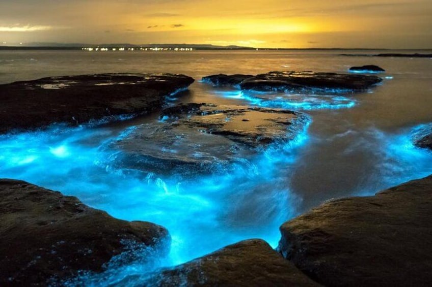 A coastal scene with illuminated water flowing over rocks at sunset. 4