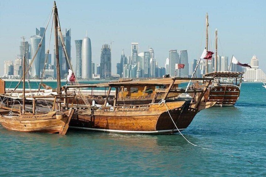 Des bateaux en bois traditionnels sont amarrés dans une marina, avec le profil moderne d’une ville en toile de fond. 3