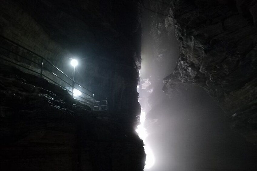 A cave entrance with a metal railing and a light source. 2