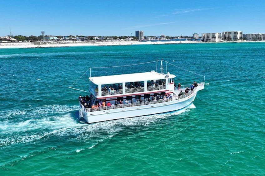 A white boat with passengers on a turquoise sea, with a beach and buildings in the background. 1