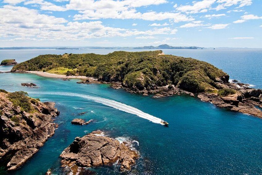 A boat navigating a narrow waterway between rocky outcrops and a lush green island. 2