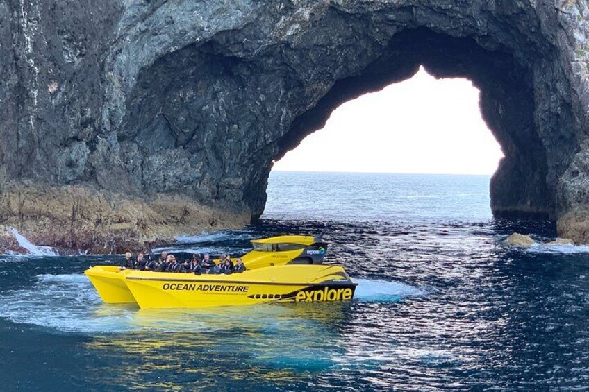 A yellow boat named 'Ocean Adventure' passing through a natural rock arch in the ocean. 1