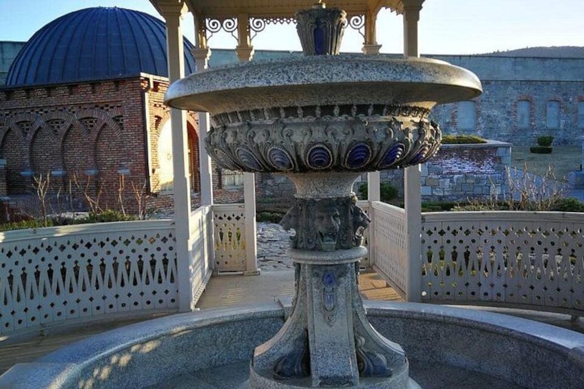 A fountain with intricate designs, a dome-shaped building, and a white fence in the background. 3