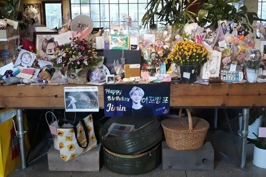 A table with various items including a 'Happy Birthday Jin'in' sign, flowers, and personal memorabilia. 5