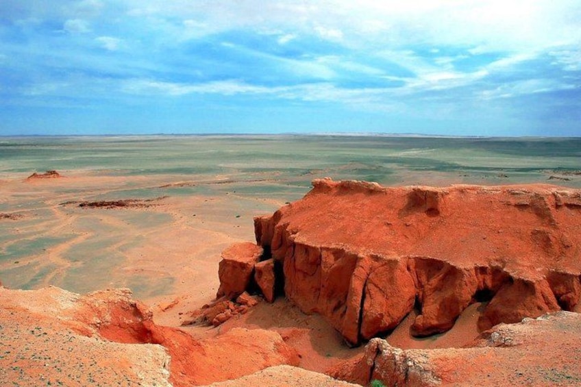 A desert landscape with a prominent red rock formation and a vast body of water. 1