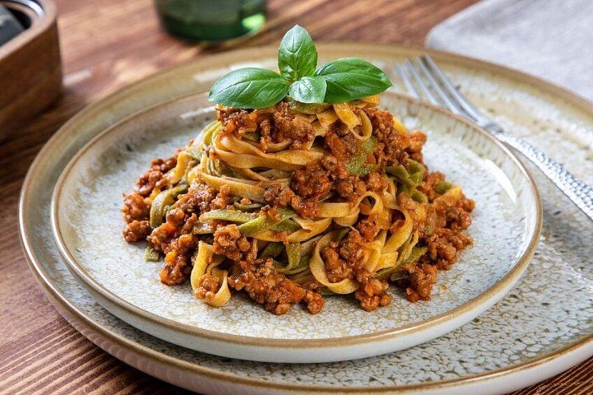 En tallrik pasta med en köttfärssås och garnerad med basilika. 5