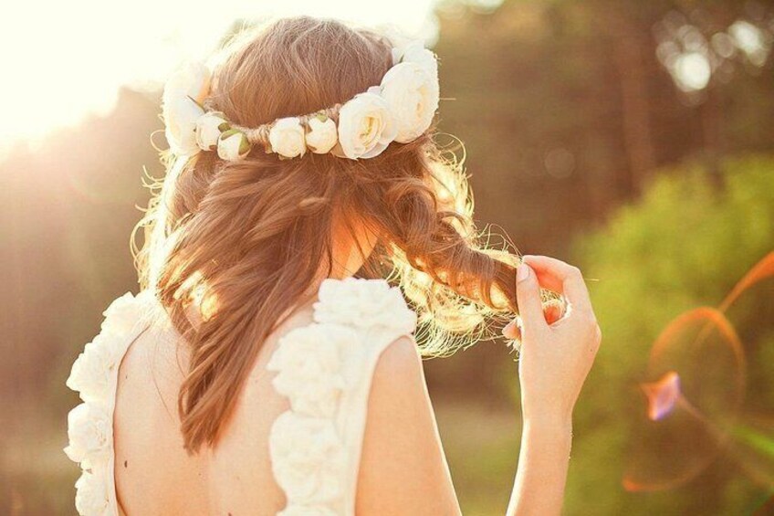 A person with a floral headpiece, wearing a white dress, outdoors with greenery in the background. 2