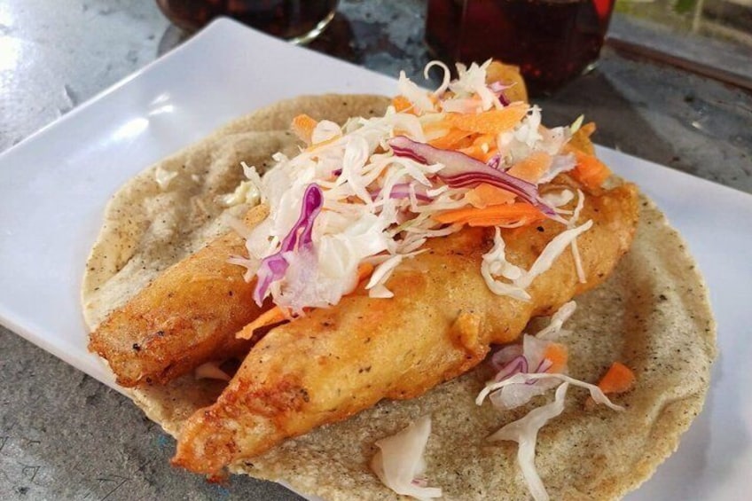 Un piatto con un taco di pesce, guarnito con cavolo cappuccio e carote grattugiate. 4