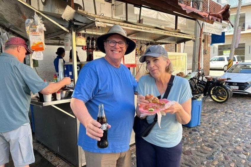 Due persone che tengono cibo e bevande a un banco di street food. 3