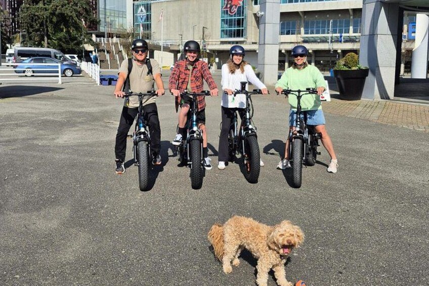 Four people on electric bikes, a dog, and a building with a sign. 2