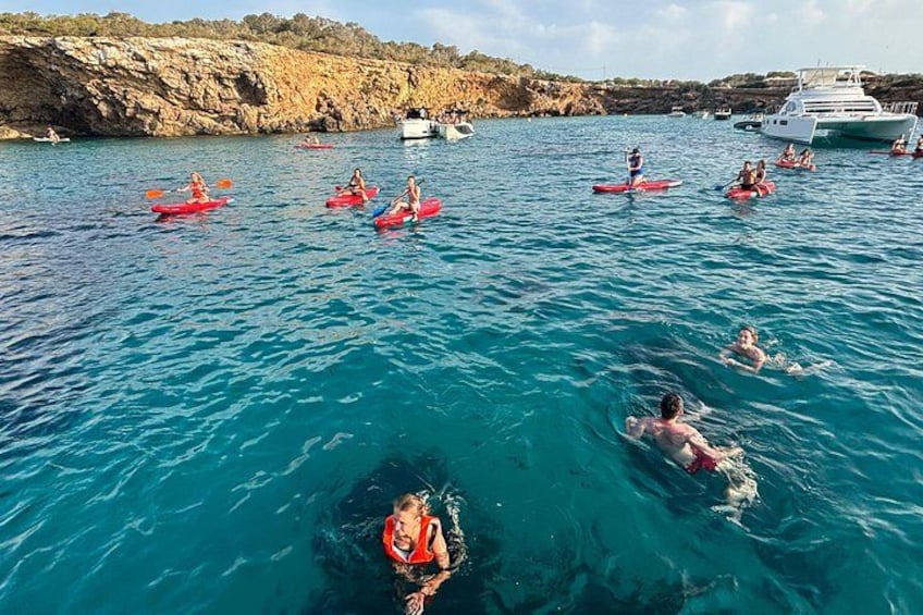 People kayaking and swimming in a clear blue sea with boats in the background. 5