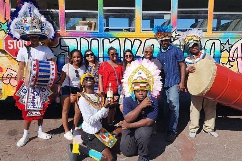 A group of people in traditional costumes, a bus with graffiti, and a large red drum. 2