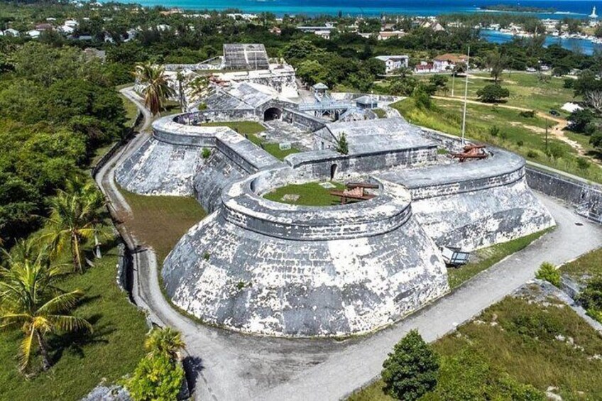A large, circular fort with multiple levels and a surrounding wall, surrounded by lush greenery and a coastal view. 3