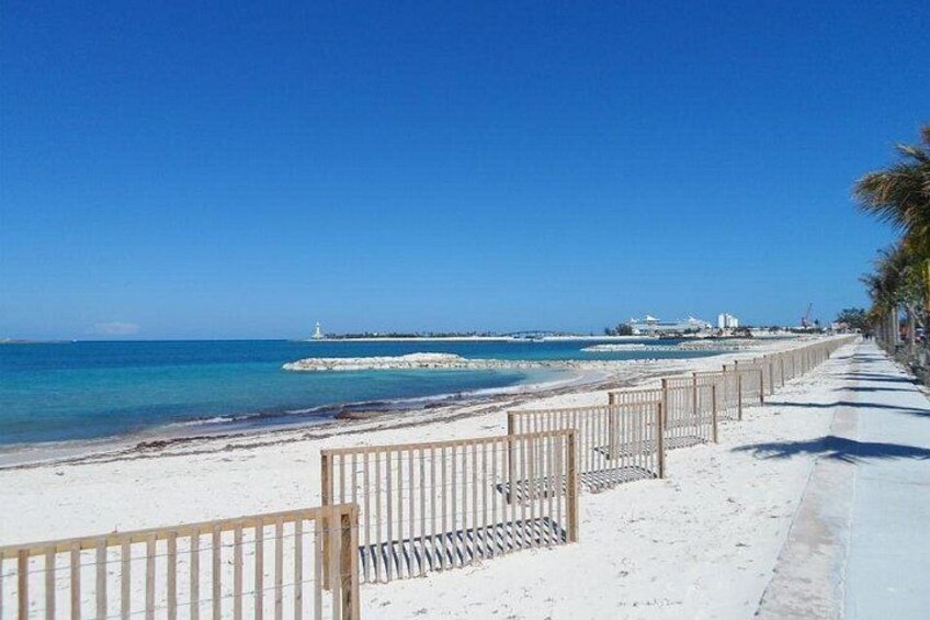A sandy beach with a wooden fence, clear blue water, and a distant lighthouse. 3
