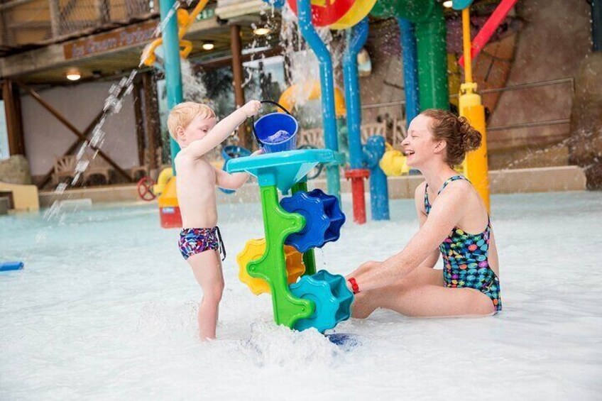 Un enfant qui joue avec de l’eau dans une piscine, une structure de jeux aquatiques et un adulte assis à proximité. 3