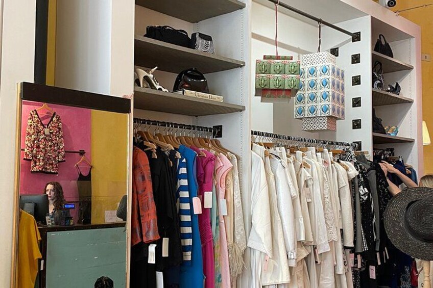 A clothing store with racks of clothes, shelves with shoes, and a hanging lamp. 1