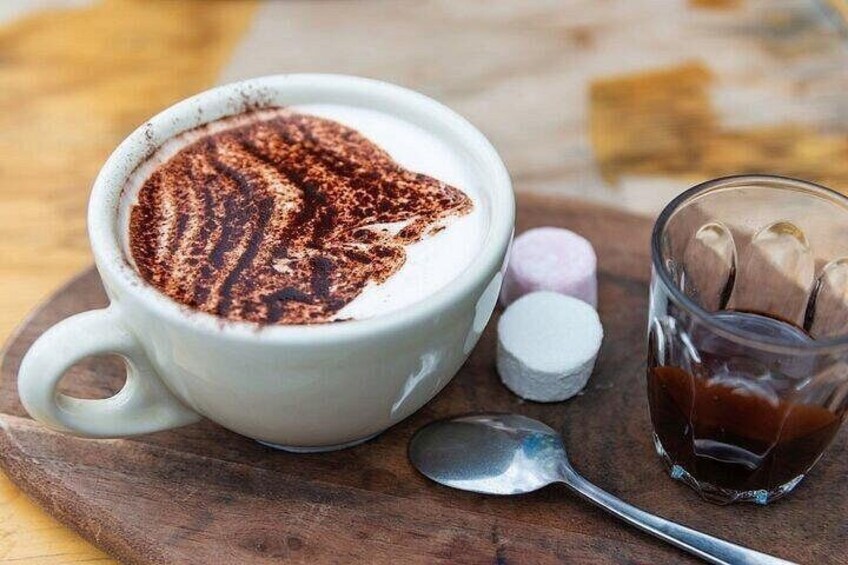 Una taza de café con espuma, una cuchara, un vaso de agua y algunos malvaviscos sobre una superficie de madera. 1