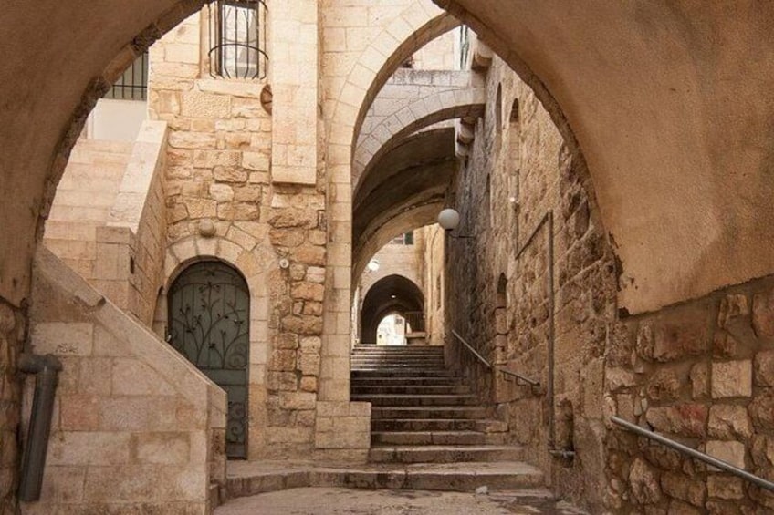 Un escalier en pierre dans une ruelle étroite, bordée d’arches, et une porte ornée de motifs décoratifs. 3