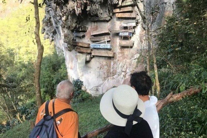 A group of people observing a large rock formation with wooden structures attached to it. 2
