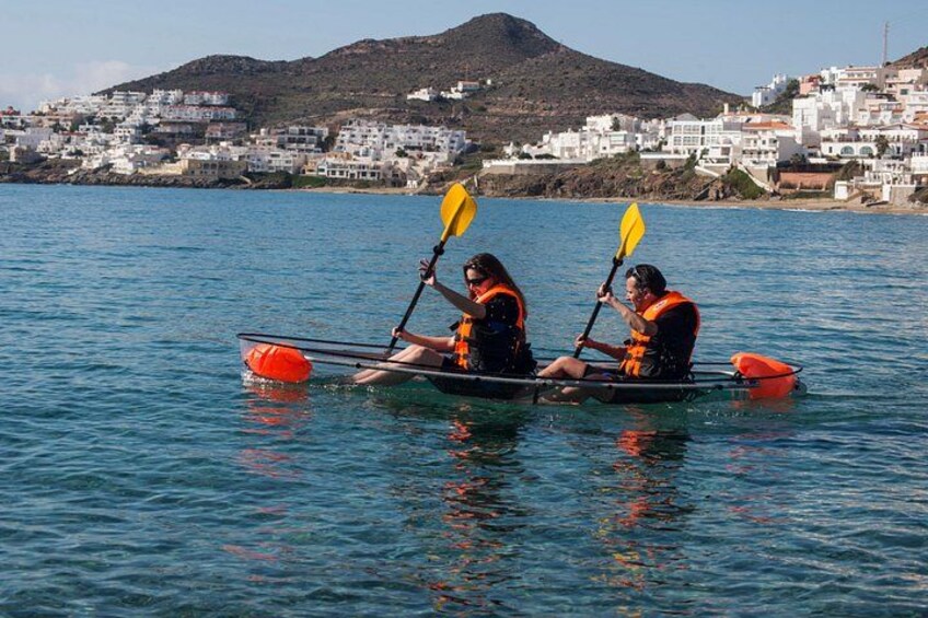Two people kayaking on calm water with a coastal town in the background. 4