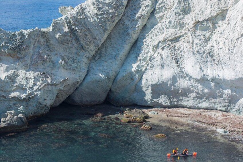 A white rock formation, clear blue water, and a person in a kayak. 3
