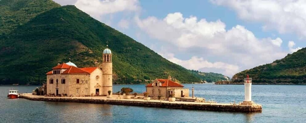 A coastal church with a bell tower, a lighthouse, and a mountainous backdrop. 2
