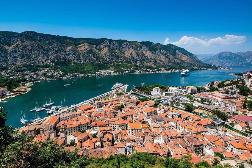 A coastal town with red-roofed buildings, a marina with boats, and mountains in the background. 4