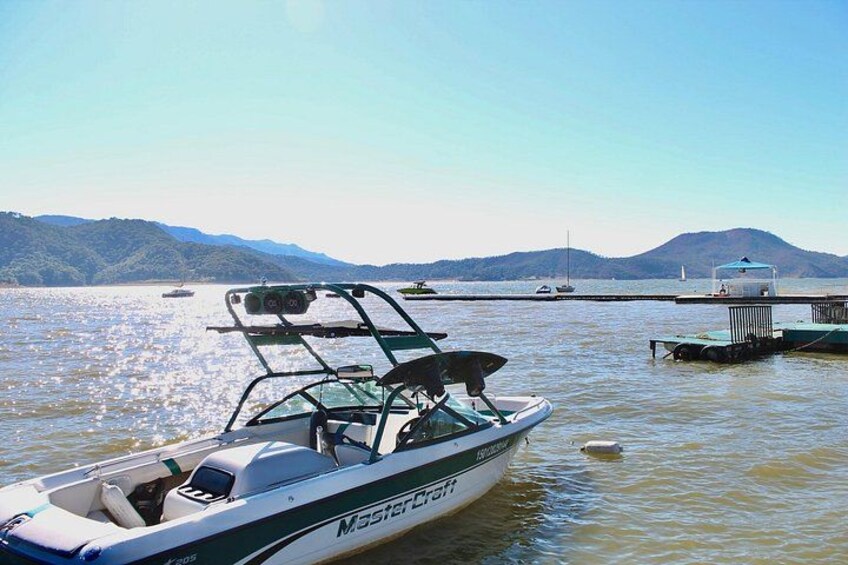 Een boot genaamd 'Mastercraft' afgemeerd aan een steiger, met rustig water en bergen op de achtergrond. 2