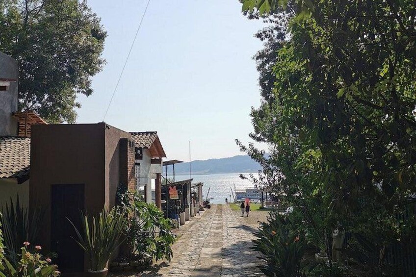 Un sendero pavimentado que conduce a un cuerpo de agua, bordeado por edificios y vegetación. 2