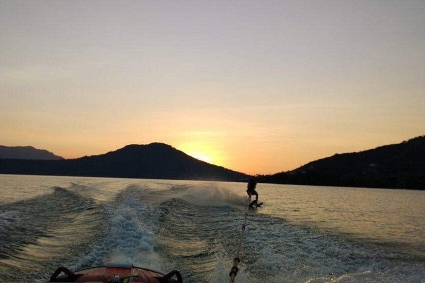 Una persona practica wakeboard en un lago con montañas al fondo durante el atardecer. 1