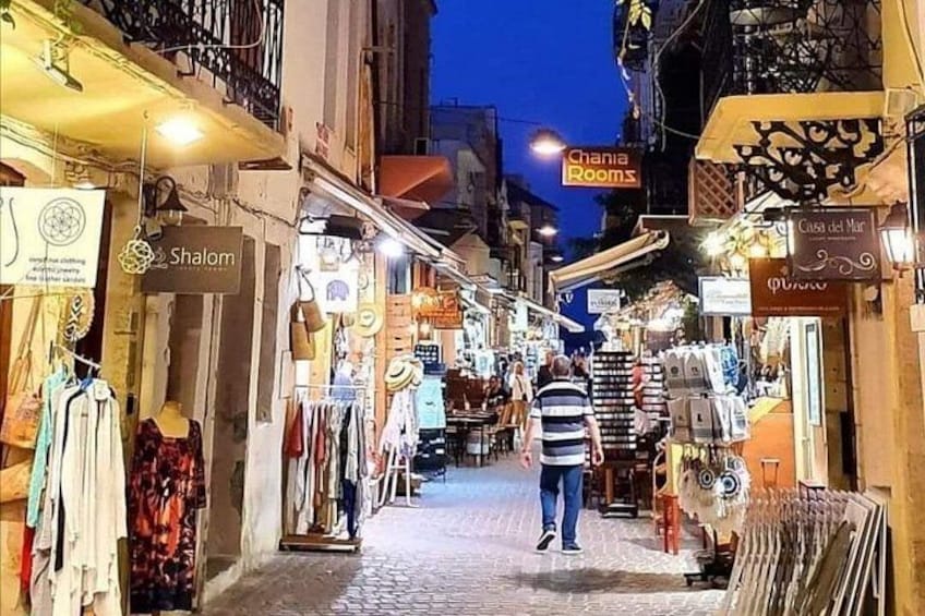 A narrow street with shops on either side, including 'Shalom' and 'Chania Rooms'. 2
