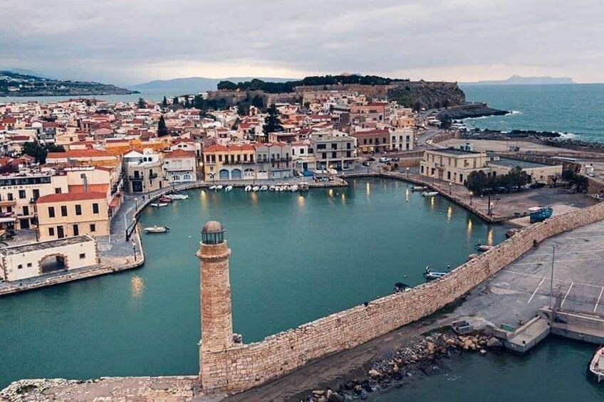 A coastal town with a prominent tower, a harbor with boats, and a fortified wall. 1