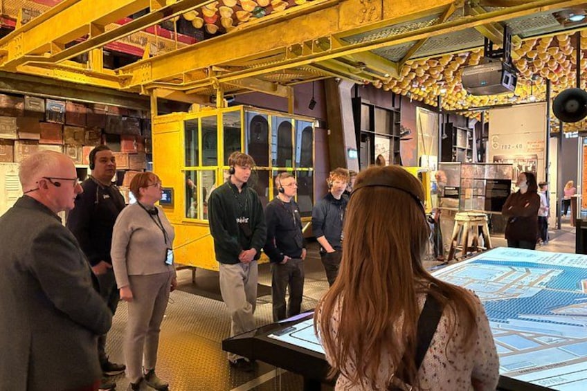 Een groep mensen in een overdekte tentoonstellingsruimte met een gele constructie en een grote kaart. 2