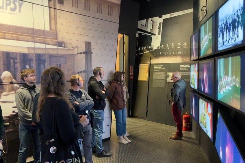 Een groep mensen staat in een museum of tentoonstellingsruimte en bekijkt objecten aan de muren. 3