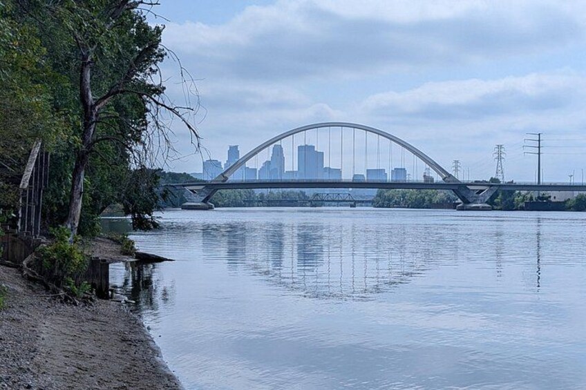 A river with a bridge, trees, and a city skyline in the background. 1