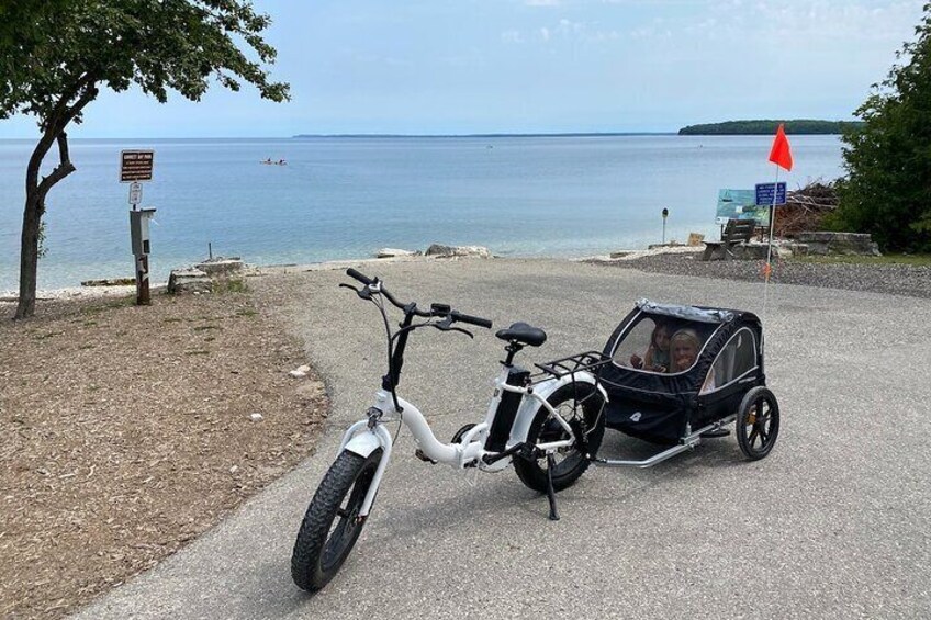 A white bicycle with a child seat attached, parked on a gravel path by the sea. 5
