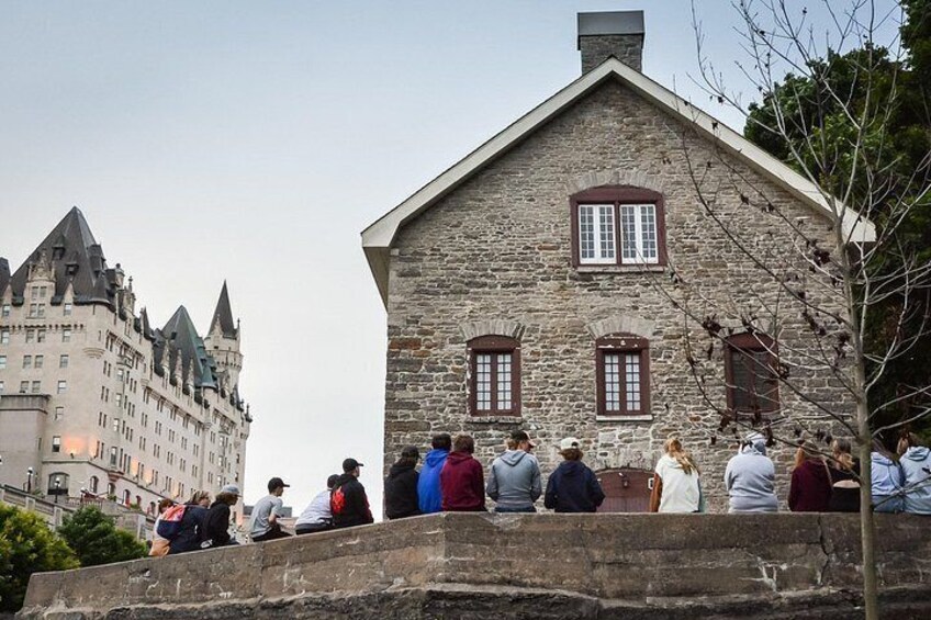 Un edificio de piedra con ventanas arqueadas y un grupo de personas sentadas sobre un muro de piedra. 3