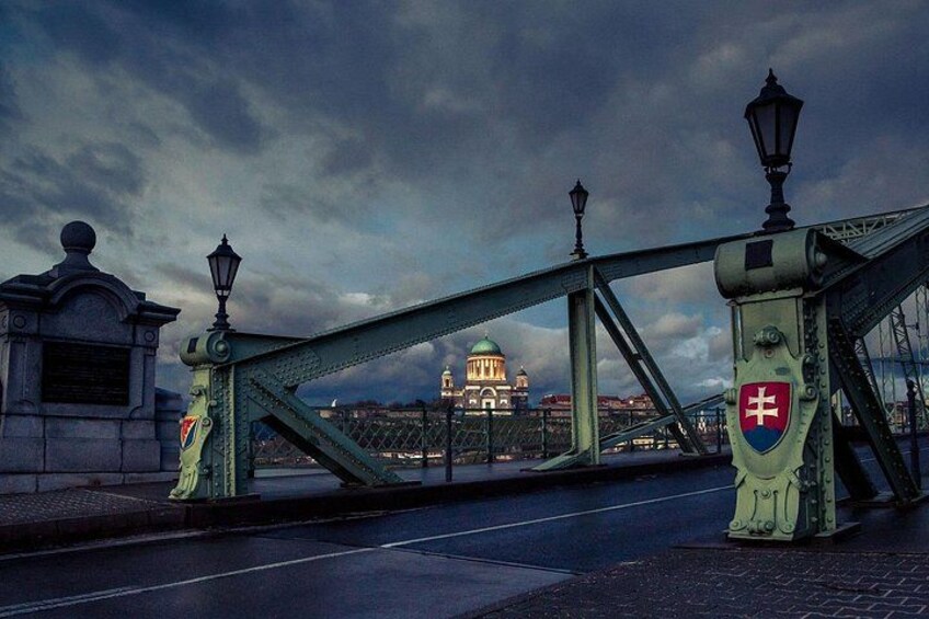 A bridge with a coat of arms, a statue, and a building in the background. 4