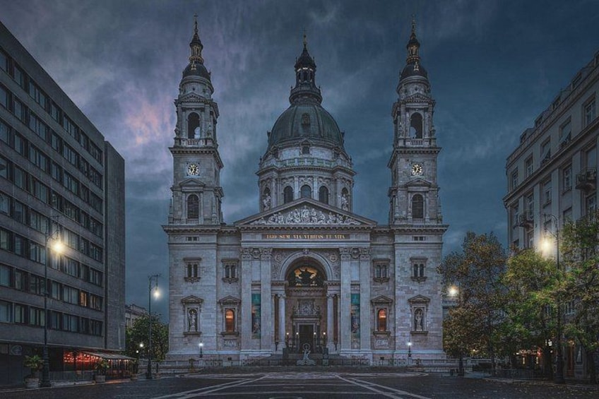 A historic building with two towers and a dome, surrounded by modern buildings. 1