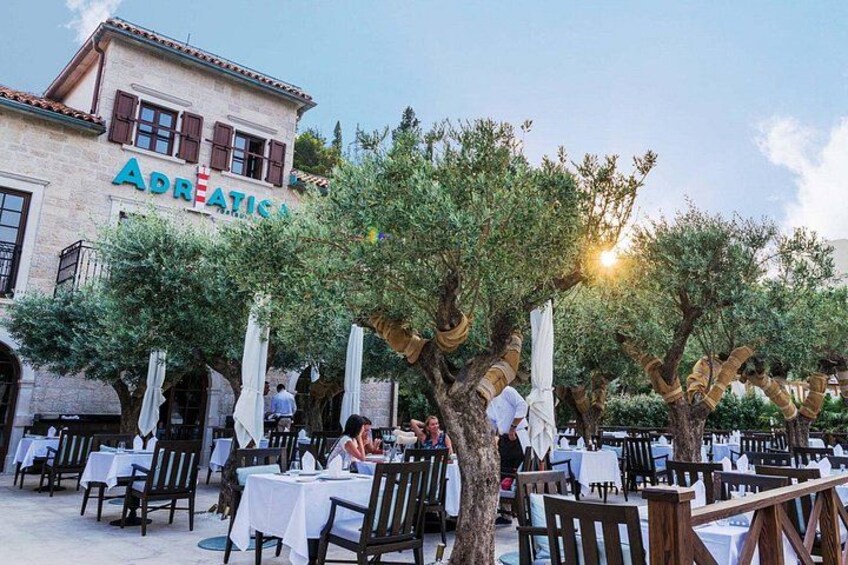 An outdoor dining area with tables and chairs, olive trees, and a building with the sign 'Adreatic.' 4