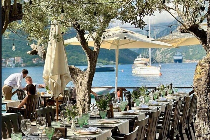 An outdoor dining area with tables and chairs, umbrellas, and a view of the sea with boats in the background. 1