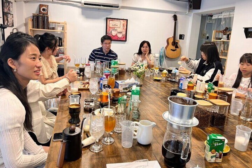 Un grupo de personas sentadas alrededor de una mesa de madera, con diversas bebidas y alimentos. 2
