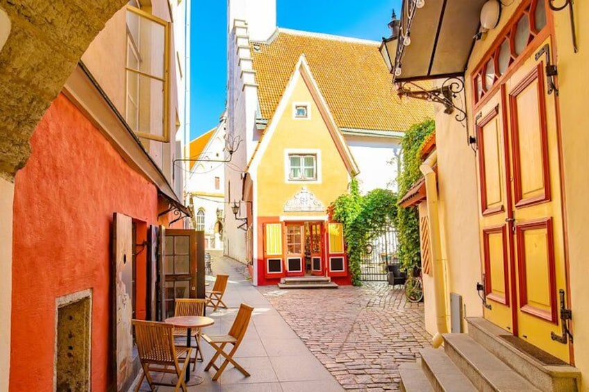 A cobblestone street with a yellow building, red doors, and a table with chairs. 3