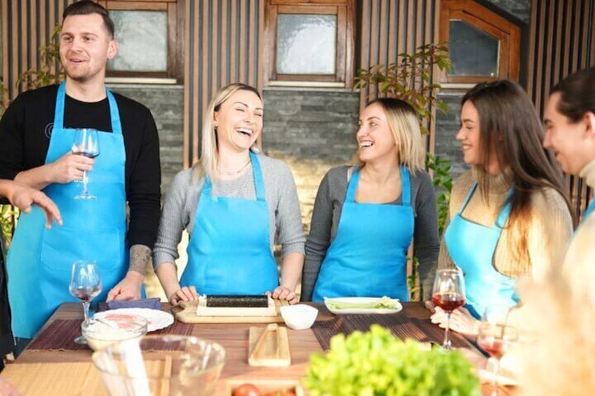 A group of people wearing aprons around a table with food and wine glasses. 1