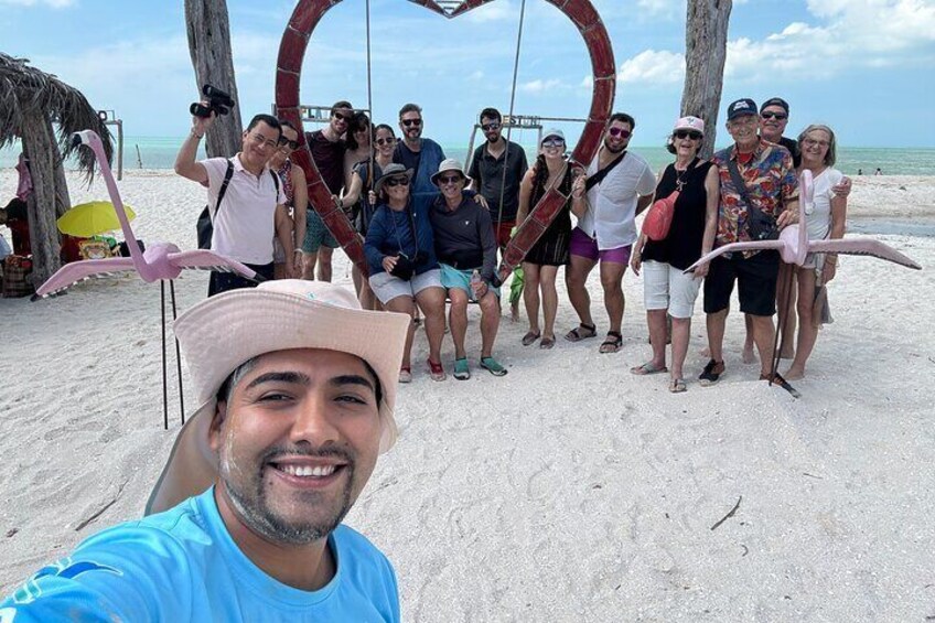 A group of people on a sandy beach with a large red heart-shaped structure in the background. 1