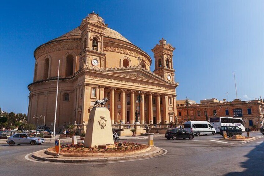 A historic building with a dome and bell towers, surrounded by a roundabout with vehicles. 5