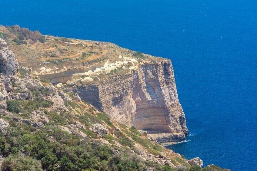 A coastal cliff with layered rock formations and sparse vegetation. 2