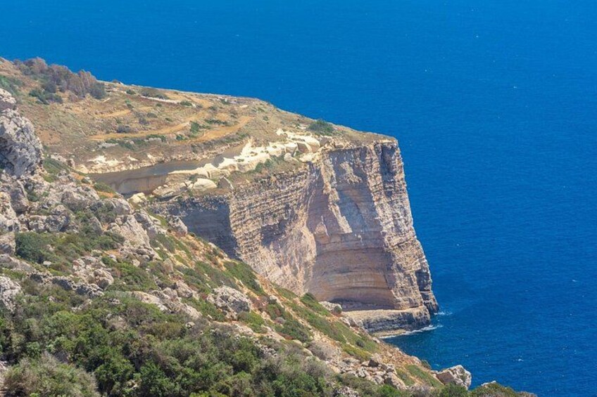 A rugged cliff with a steep drop into the ocean, surrounded by sparse vegetation and rocky terrain. 2