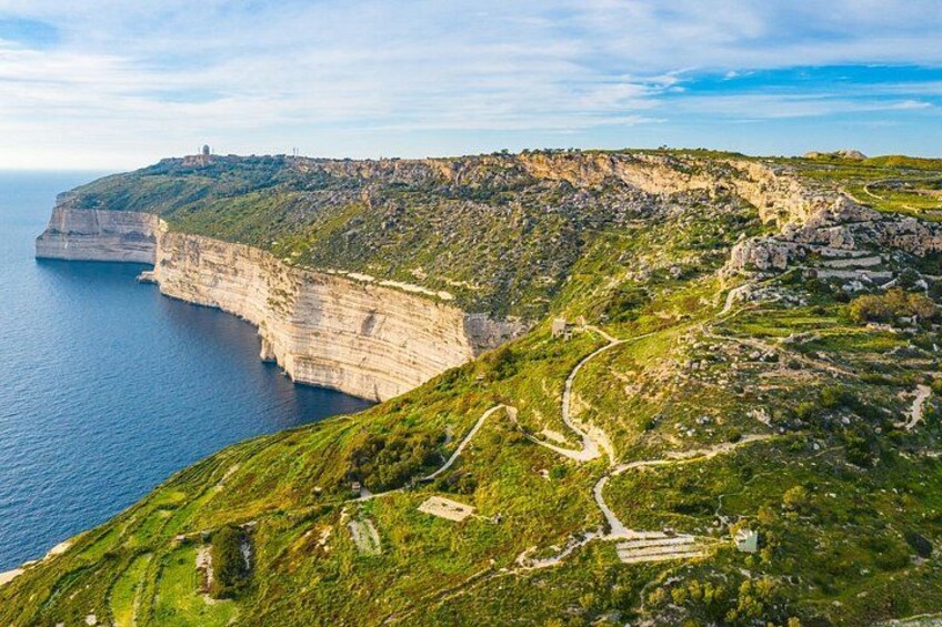 A coastal cliff with a winding path, a small settlement, and a lighthouse. 1